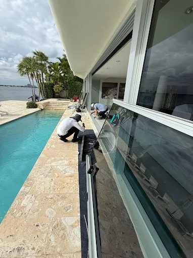 Two technicians completing a sliding glass door installation beside a waterfront pool